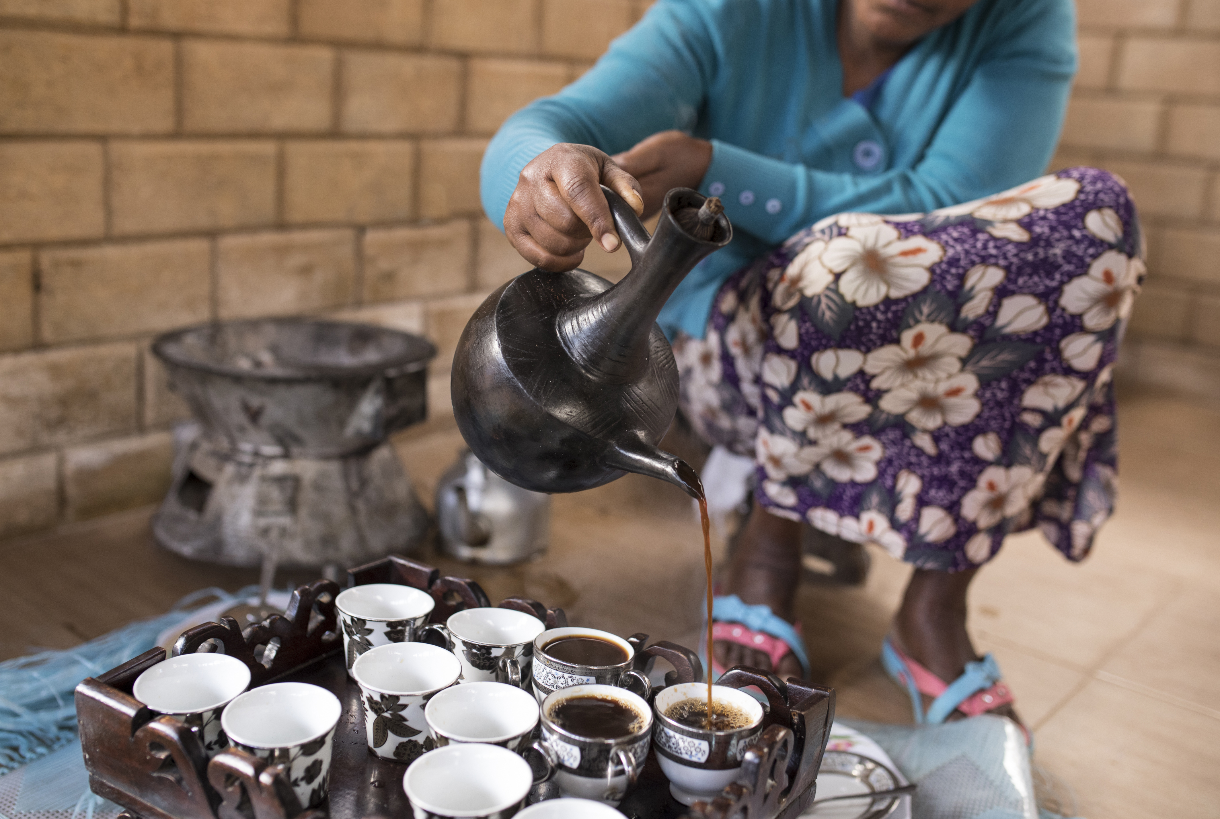 Ethiopian woman performing a traditional coffee ceremony with jebena on a charcoal stove, frankincense burning nearby