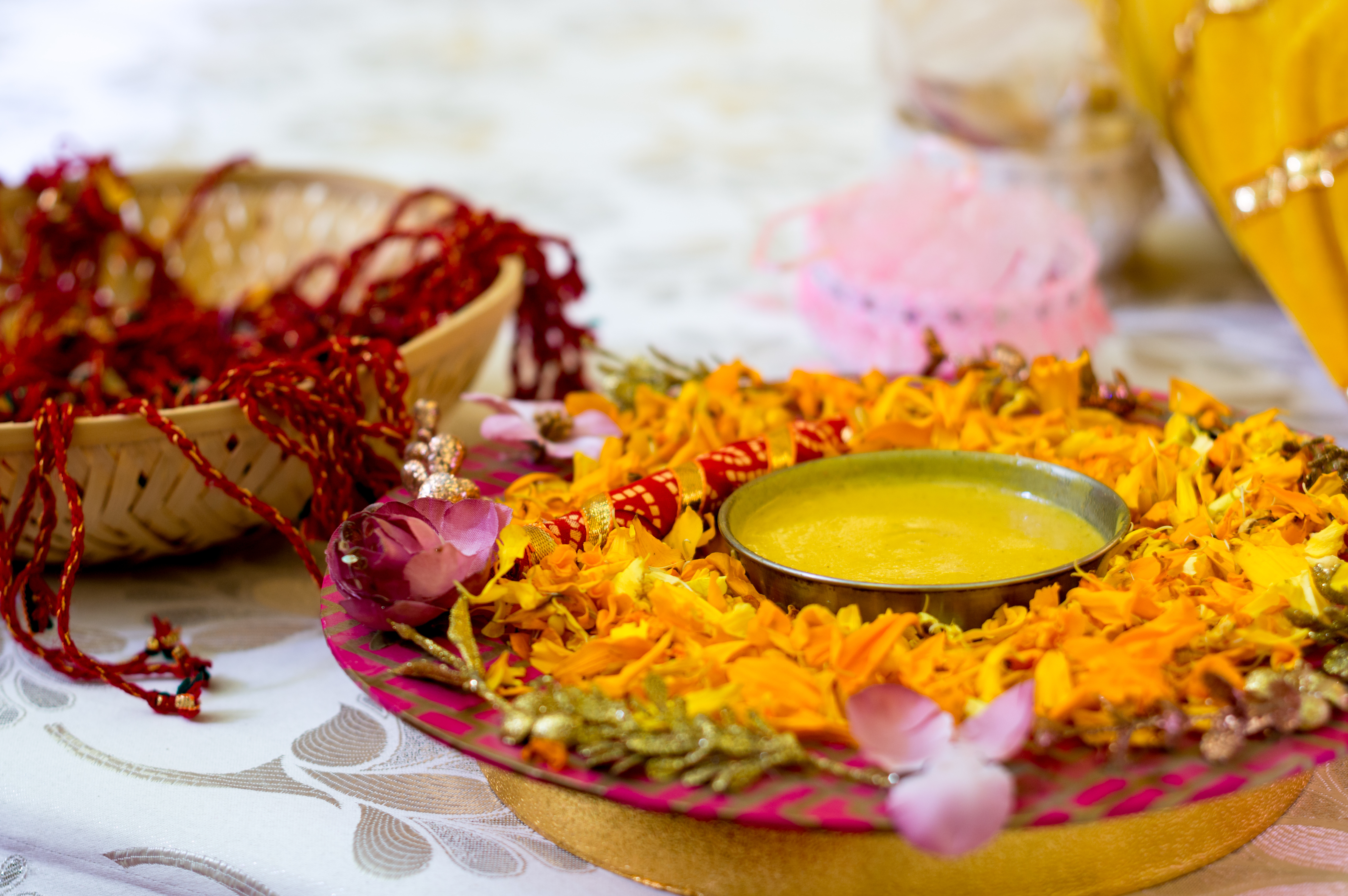Decorated brass bowl of haldi paste with rose petals and mango leaves on a floral thali