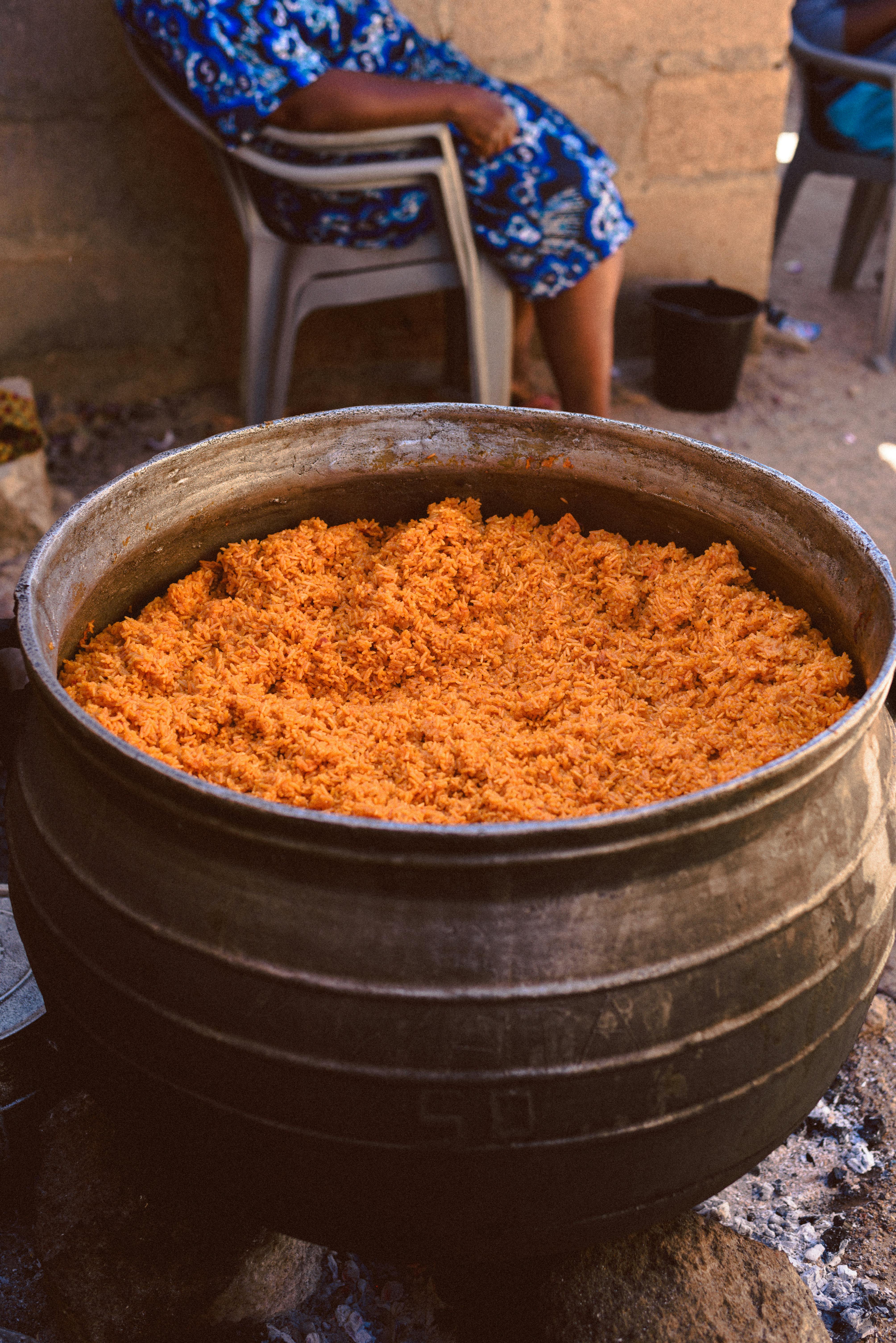 Chef preparing large pots of party jollof rice for a Nigerian wedding, steam rising