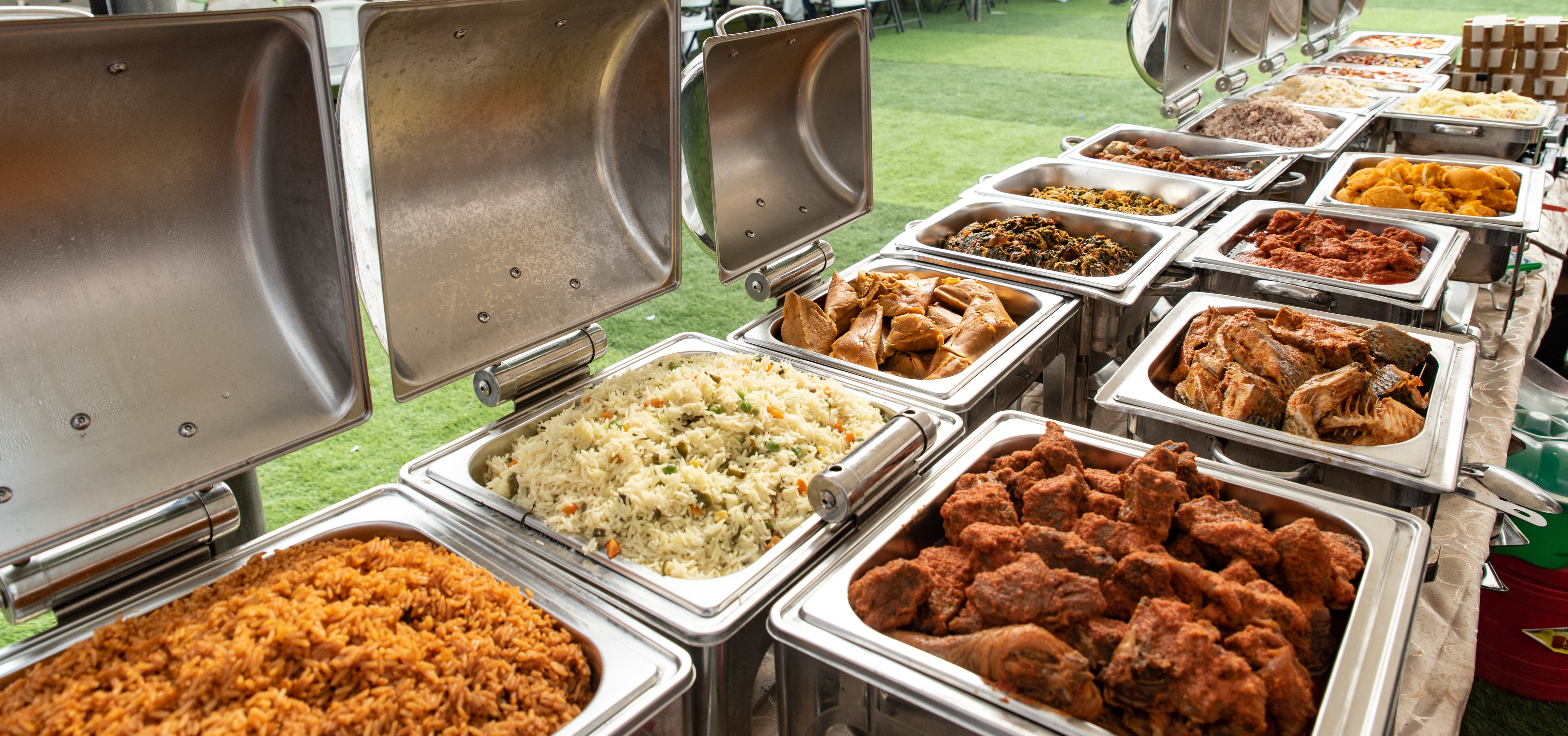 Spread of Nigerian wedding food including jollof rice, small chops, and assorted proteins on decorated serving tables